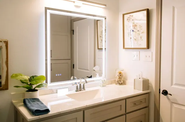 Greige vanity under a backlit mirror with a potted plant