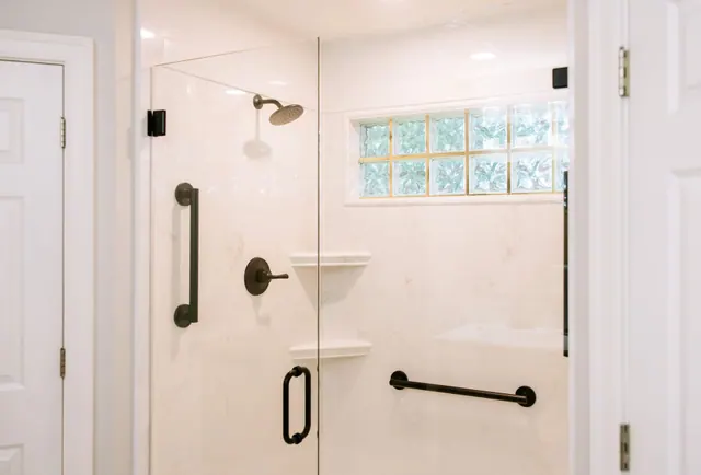 Walk-in shower with a corner shelf, handheld wand and two grab bars
