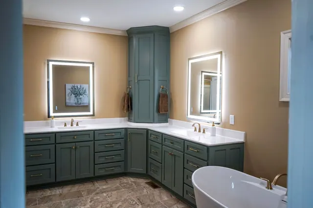 Teal corner vanity with two lit mirrors beside a freestanding tub