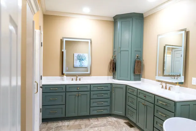 Teal tall storage cabinet between two vanities with backlit mirrors