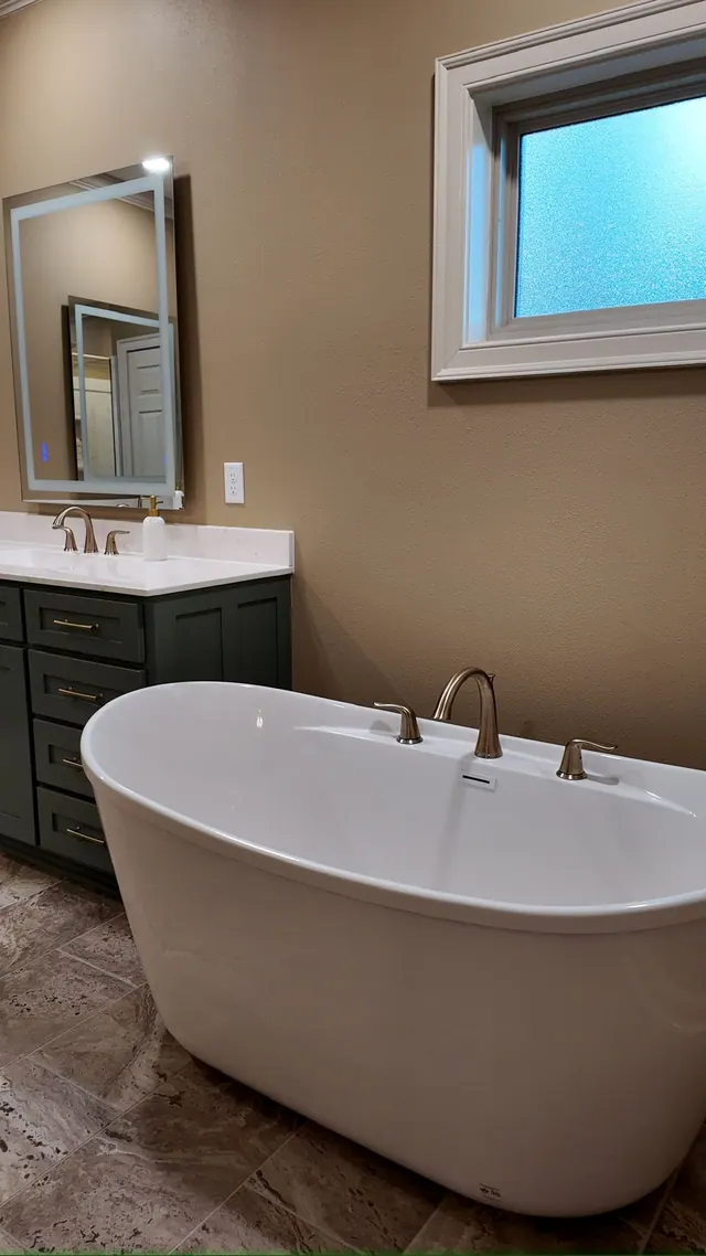 Freestanding tub under a window beside teal cabinetry