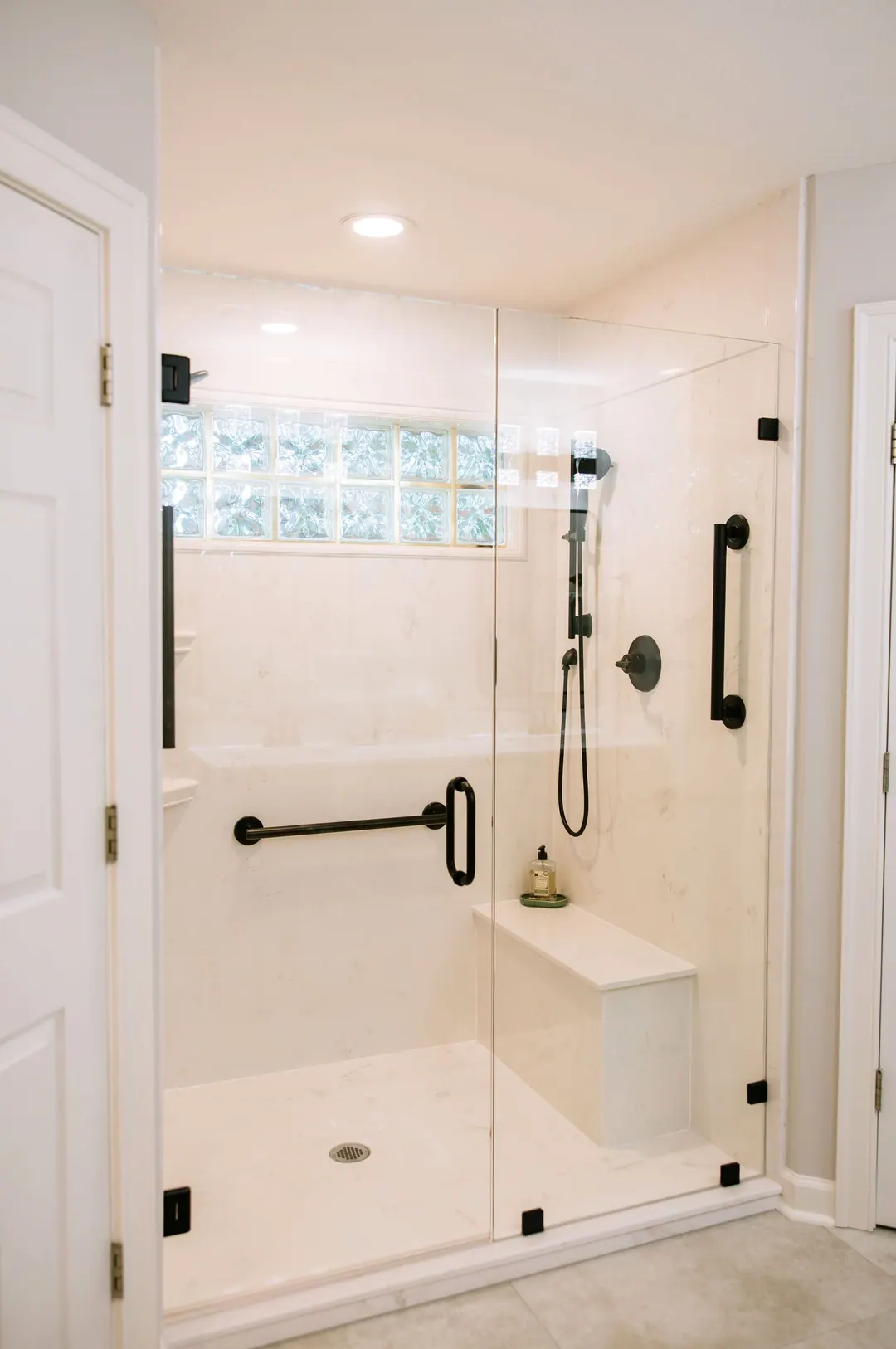 Walk-in shower with frameless glass, a built-in bench and black grab bars