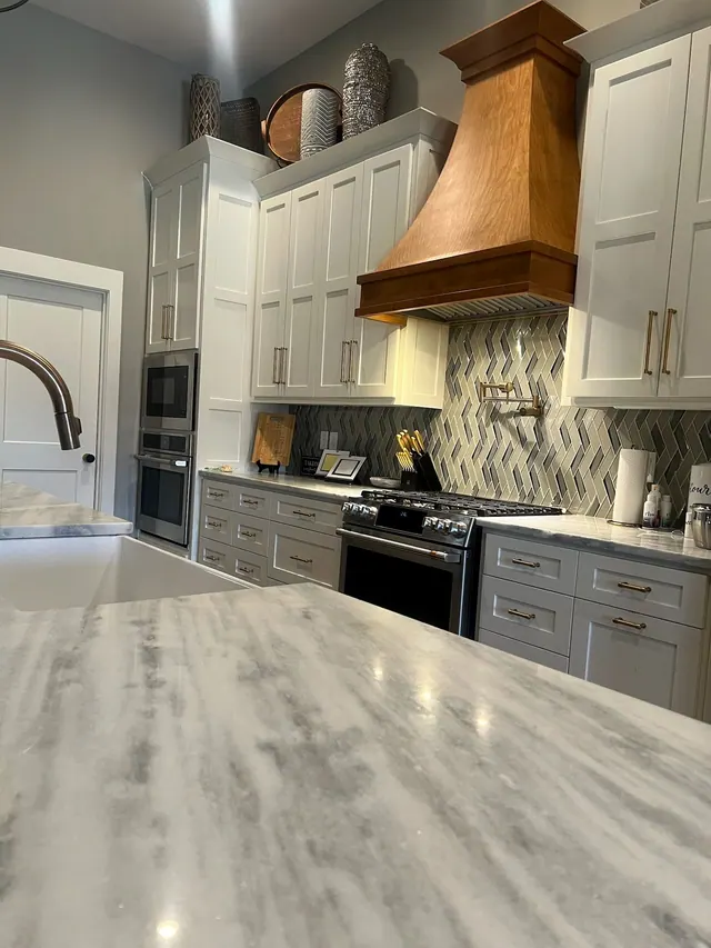 Kitchen with a wood range hood, herringbone backsplash and grey island