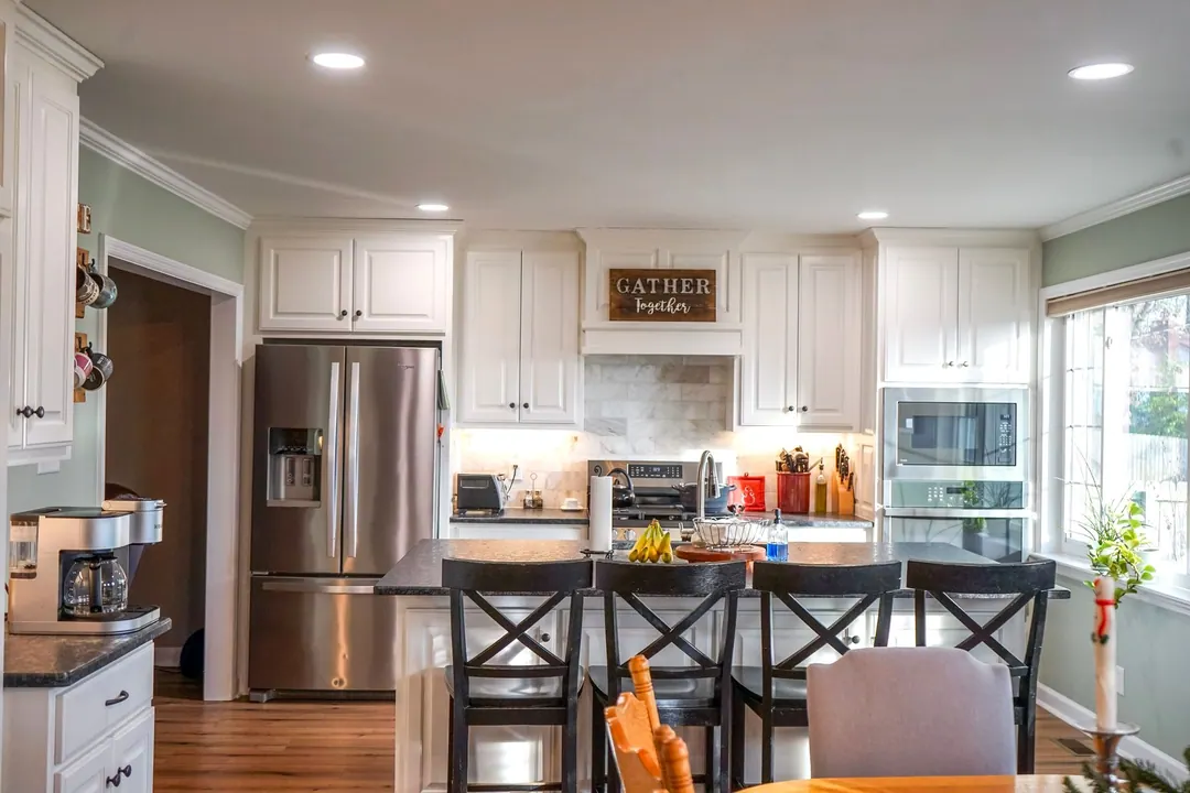White kitchen opening to a dining table with a Gather sign above the range