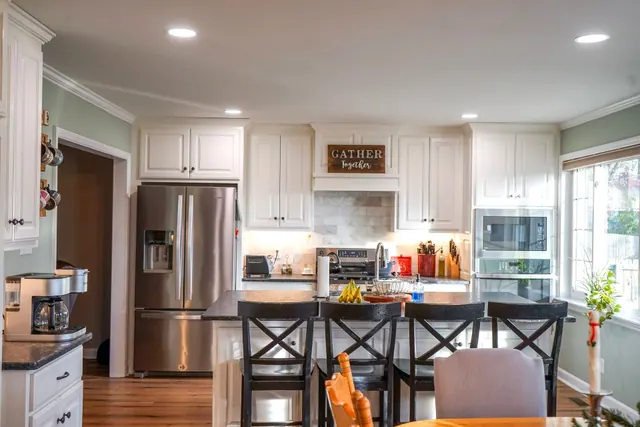 White kitchen opening to a dining table with a Gather sign above the range