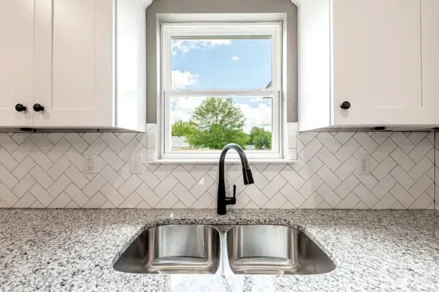 Double sink under a window with a herringbone tile backsplash