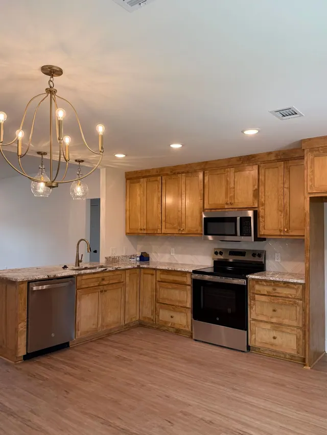 Maple kitchen with stainless appliances under a brushed chandelier