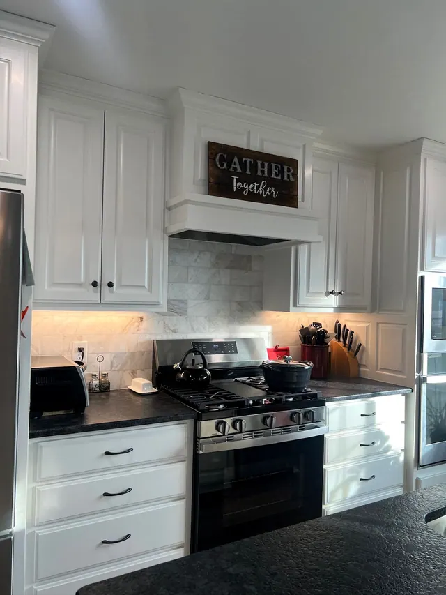 White cabinets around a black range with a farmhouse sign