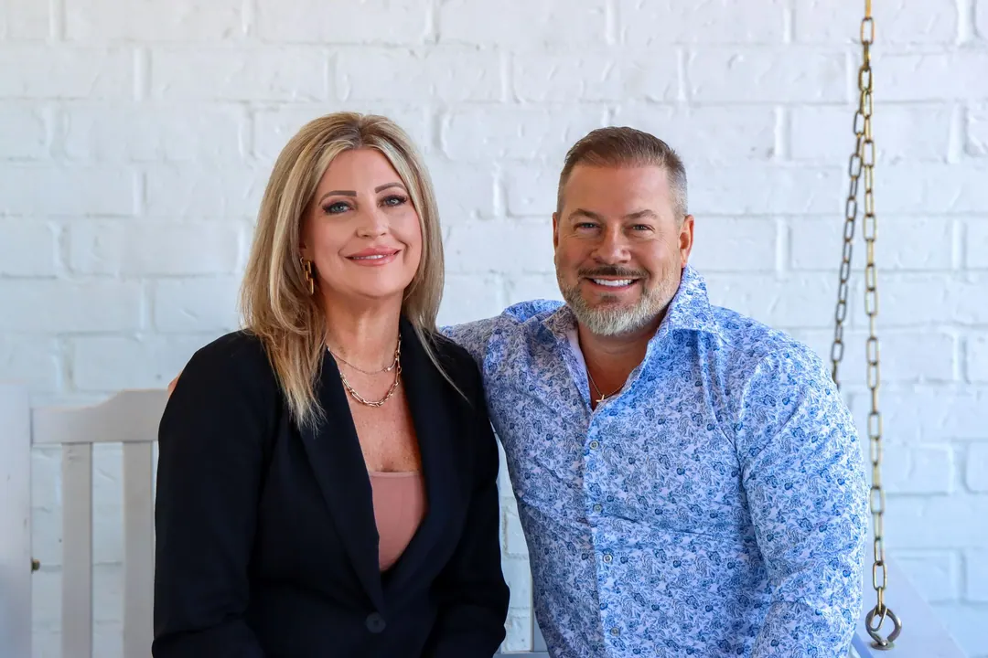 Scott and Cindy Lucas on a porch swing against white brick